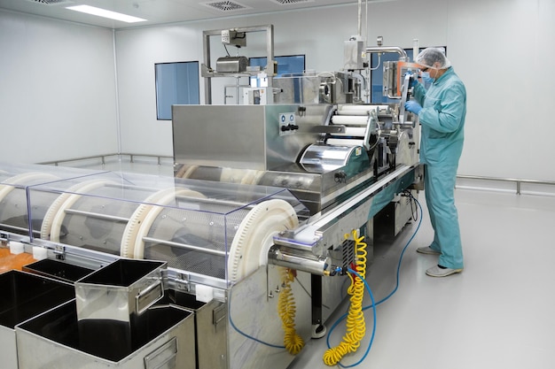 Pharmacy industry factory man worker in protective clothing in sterile working conditions operating on pharmaceutical equipment