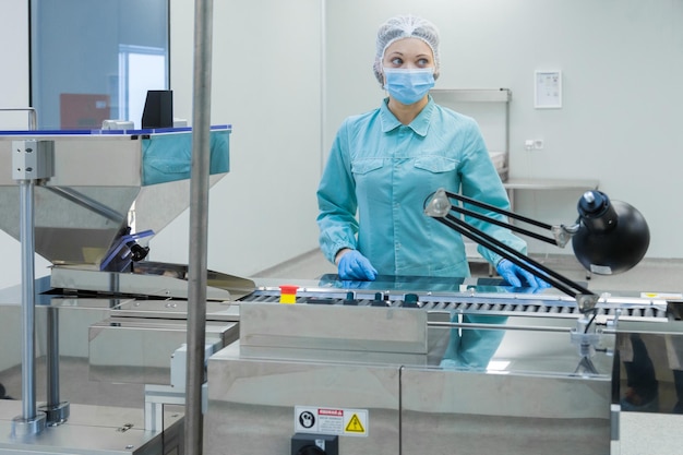 Pharmacy industry woman worker in protective clothing operating production of tablets in sterile working conditions