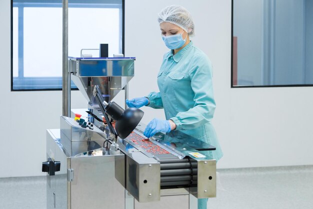 Pharmacy industry woman worker in protective clothing operating production of tablets in sterile working conditions