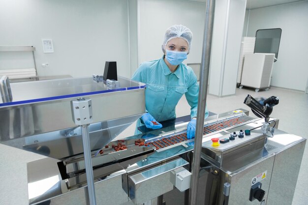 Pharmacy industry woman worker in protective clothing operating production of tablets in sterile working conditions