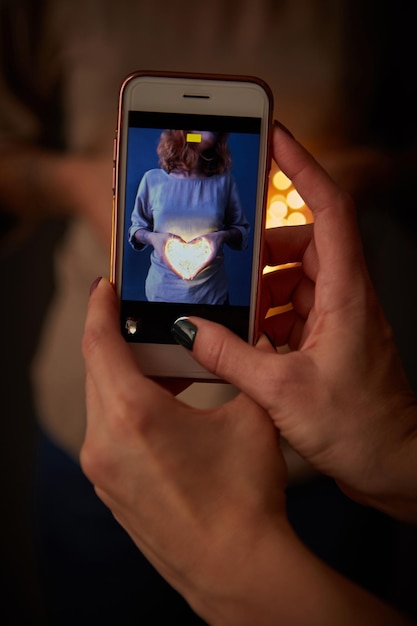 The phone with the image of a girl with a glowing heart is holding a woman in a blurred background with a beautiful bokeh