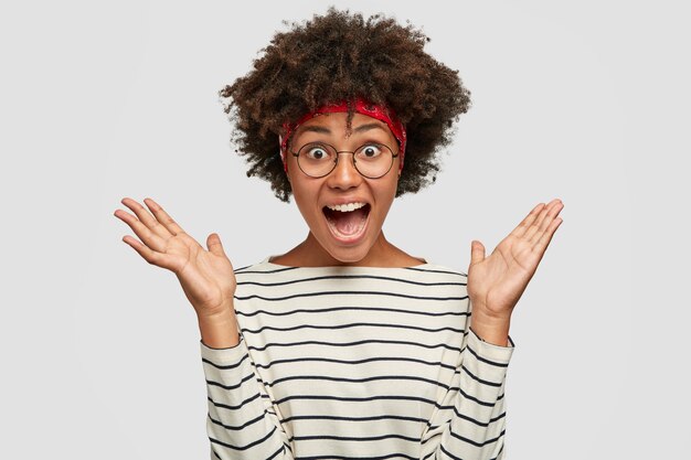 Photo of amazed surprised overjoyed black lady clasps hands, exclaims with surprised expression