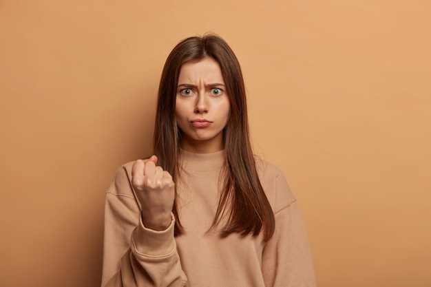 Photo of angry Caucasian woman clenches fist, comes to argue, complains about noise, looks crossly at camera