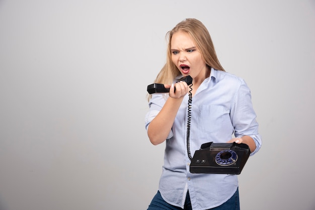 Фотография злой модели женщины, стоящей и кричащей на черный старый телефон