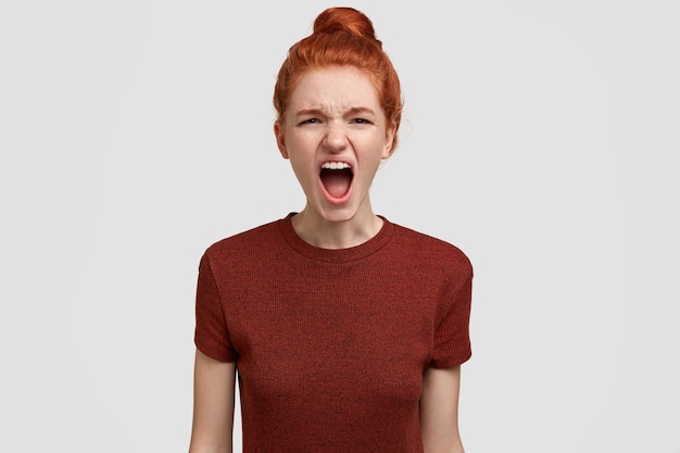 Photo of annoyed red haired female teenager screams loudly, feels irritated