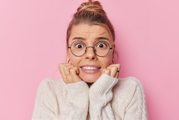 気になるストレスのたまった女性の写真は、おびえた表情で歯を食いしばり、あごがピンクの壁に丸い眼鏡とセーターのポーズをとっている恐ろしいものに反応し続けます。