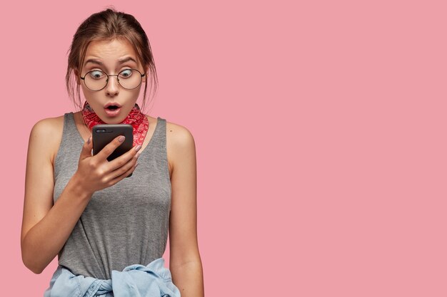 Photo of astonished teenage girl stares at screen of smart phone