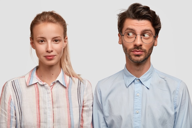 Free photo photo of attractive blonde woman with pony tail, curious unshaven guy stand shoulder to shoulder against white wall, have friendly relationships. two colleagues meet together for making project
