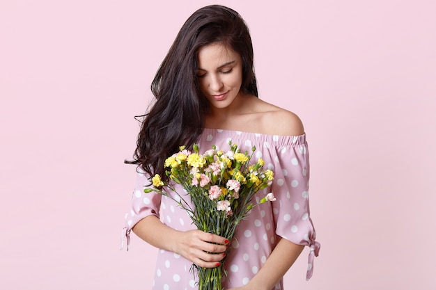 魅力的なブルネットの女性モデルの写真は春の花を保持し、水玉のドレスを着ています