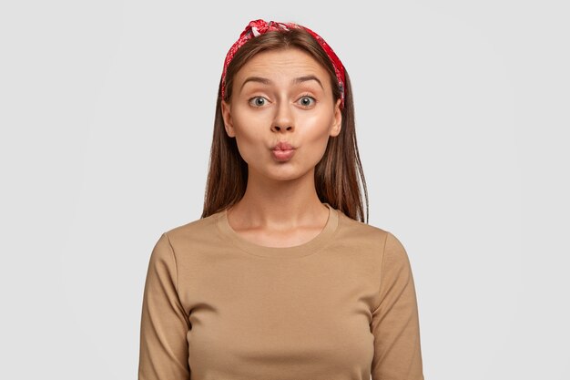 Photo of attractive Caucasian woman round lips, makes grimace, wants to kiss someone