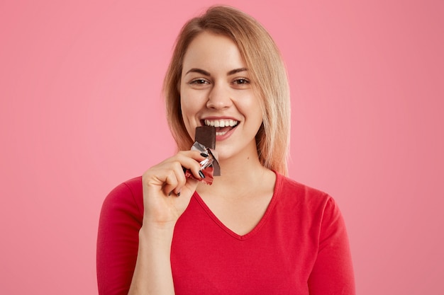 魅力的な明るい髪のヨーロッパの若い女性の写真は、甘党であるおいしい甘いチョコレートを食べる