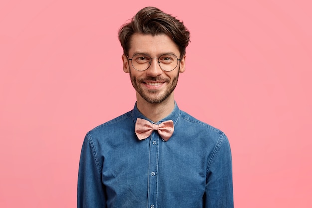 Photo of attractive smiling man with trendy hairstyle, positive look, dressed in fashionable festive outfit, stands against pink wall