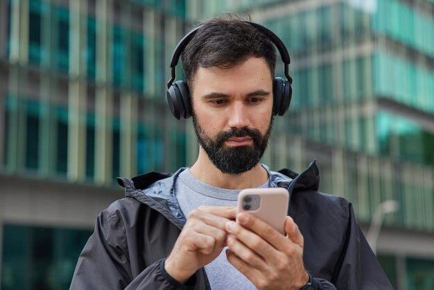 스마트폰 화면에 집중된 수염 난 남자의 사진은 음악을 듣고 자유 시간을 즐기고 재생 목록에 있는 좋아하는 노래가 있는 휴대 전화를 들고 바람막이 채팅을 온라인으로 착용