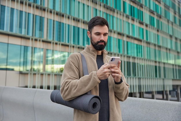 수염을 기른 젊은 스포츠맨의 사진은 휴대폰 다운로드 애플리케이션을 사용하여 문자 메시지를 보냅니다.