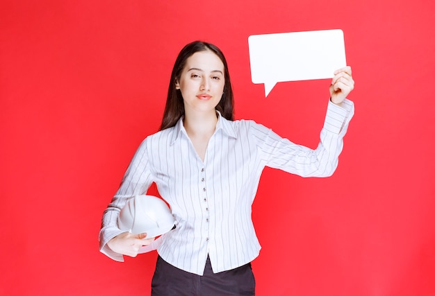 Photo of a beautiful business woman holding safety hat with empty speech bubble.