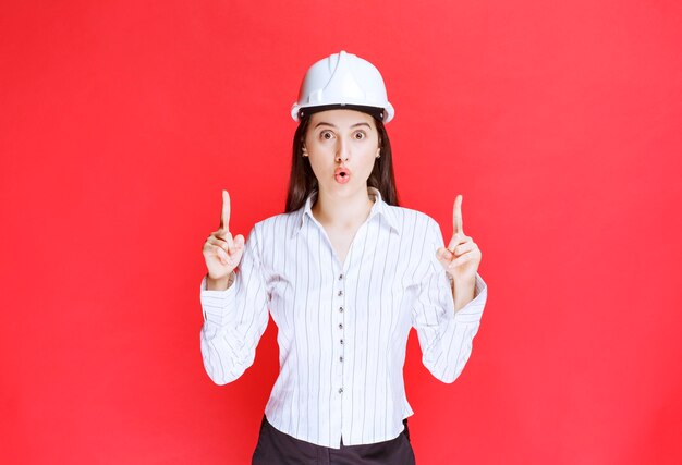 Photo of a beautiful business woman wearing safety hat pointing away with fingers.