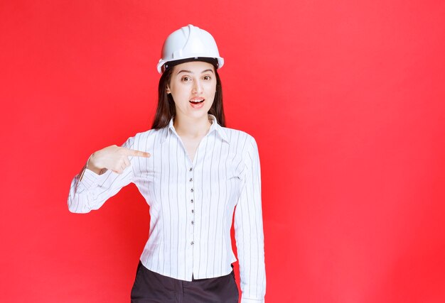 Photo of a beautiful business woman wearing safety hat pointing away with fingers.