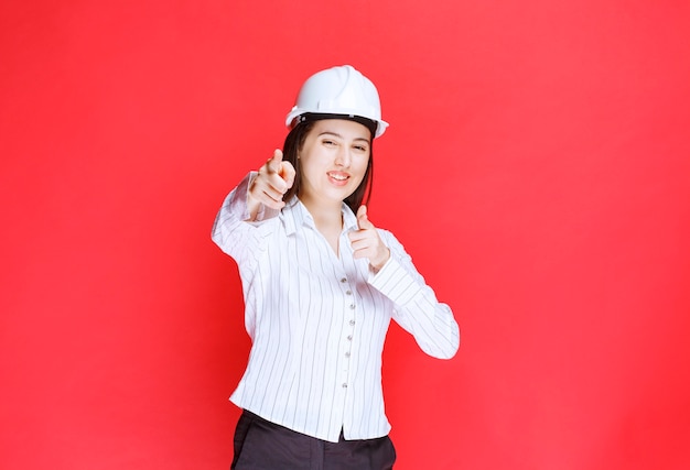 Photo of a beautiful business woman wearing safety hat pointing at camera.