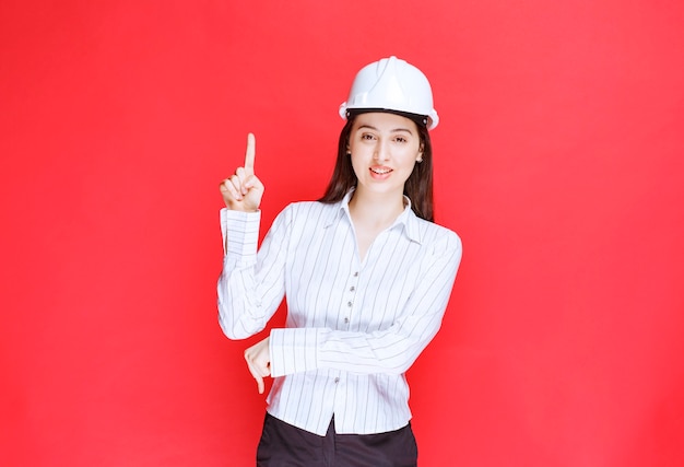 Photo of a beautiful business woman wearing safety hat pointing up.