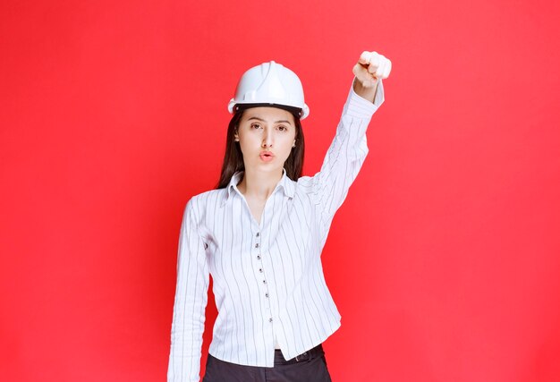 Photo of a beautiful business woman wearing safety hat standing against red wall.