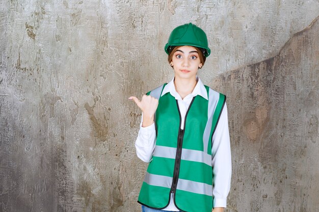 Photo of beautiful female architect in green helmet pointing