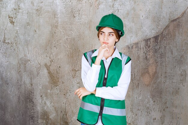 Photo of beautiful female architect in green helmet standing over marble