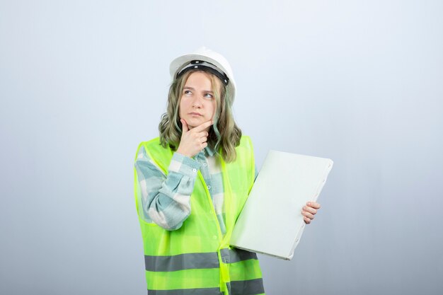 Photo of beautiful female industrial worker holding empty canvas and thinking. High quality photo