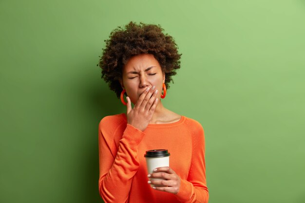 Photo of beautiful tired woman yawns and being sleepy holding a cup