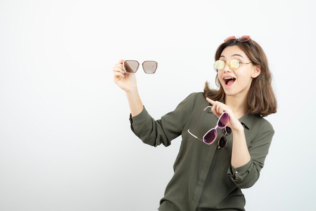 白の上にカラフルなサングラスを保持している美しい女性の写真。高品質の写真