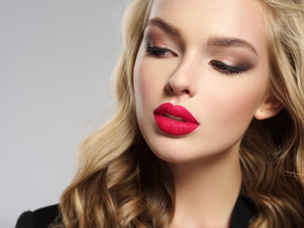 Photo of a beautiful young blond girl with sexy red lips. Closeup attractive sensual face of white woman with long hair. Smoky eye makeup