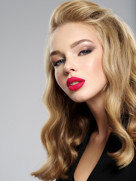 Photo of a beautiful young blond girl with sexy red lips. Closeup attractive sensual face of white woman with long hair. Smoky eye makeup