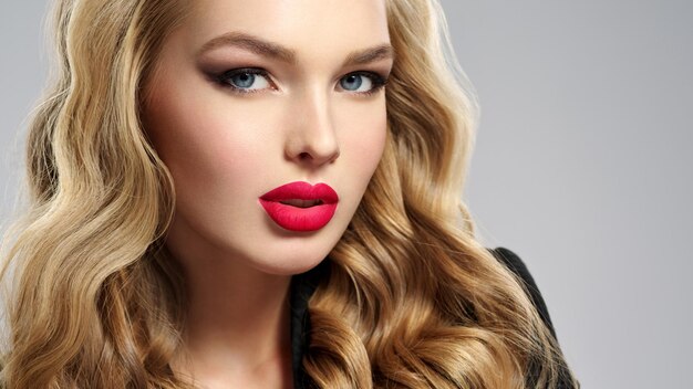 Photo of a beautiful young blond girl with sexy red lips. Closeup attractive sensual face of white woman with long hair. Smoky eye makeup