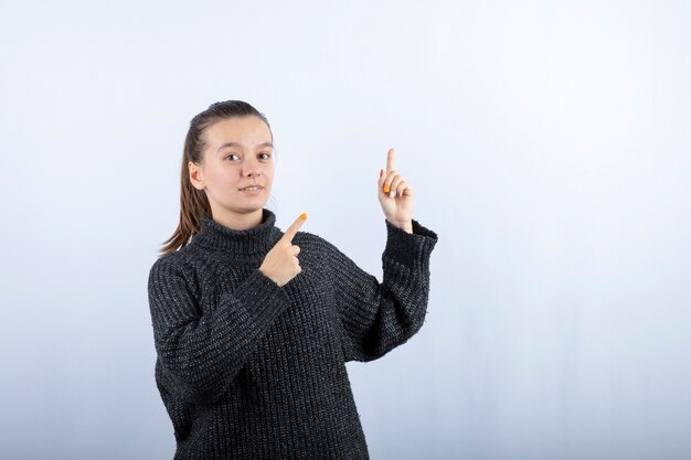 Photo of beautiful young girl pointing at somewhere on grey. 