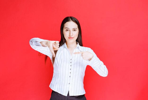 Photo of beautiful young woman in formal outfit showing thumbs down. 