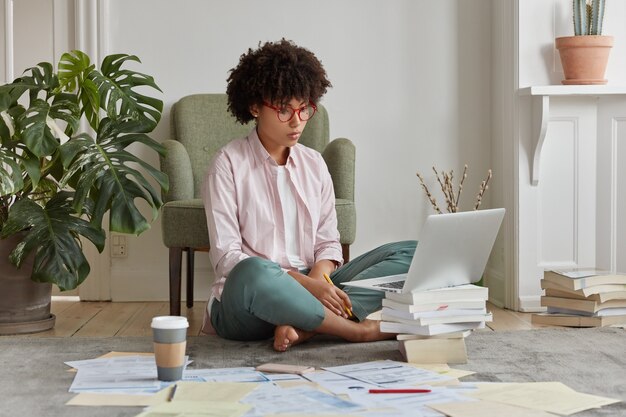 Фотография темнокожей деловой женщины, одетой в повседневную одежду, сидит скрестив ноги с графическими диаграммами, анализирует доходы компании.