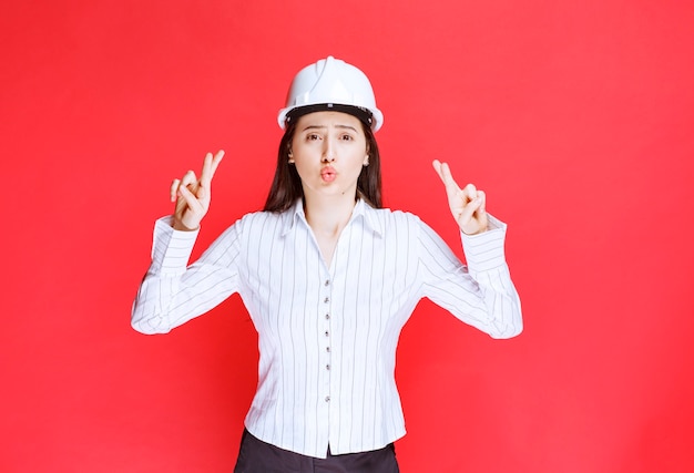 Foto gratuita foto di una donna d'affari con un cappello di sicurezza che mostra le dita incrociate.