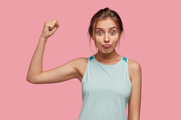 Photo of Caucasian sportswoman shows muscle, raises hands in fist