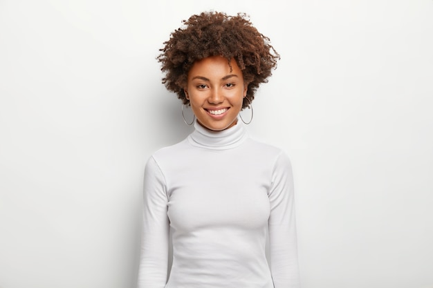 Photo of charismatic lovely woman with curly hair, has fun, toothy smile on face
