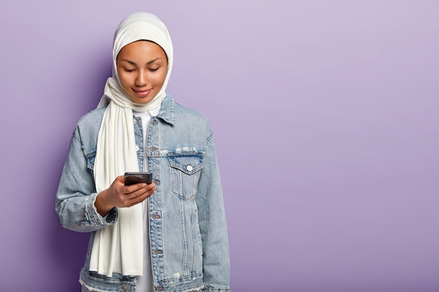Foto della signora musulmana charmimg concentrata nel moderno dispositivo smartphone