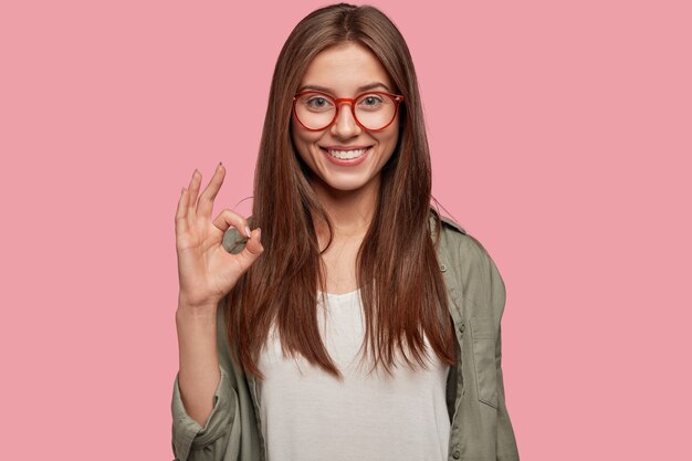 Photo of charming beautiful woman with broad smile, shows excellent sign, demonstrates that everything is fine