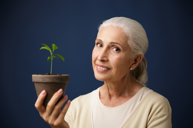 Free photo photo of cheerful aged woman holding young plant in the spot