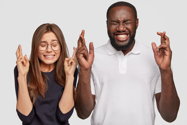 Photo of cheerful dark skinned man, positive European woman cross fingers