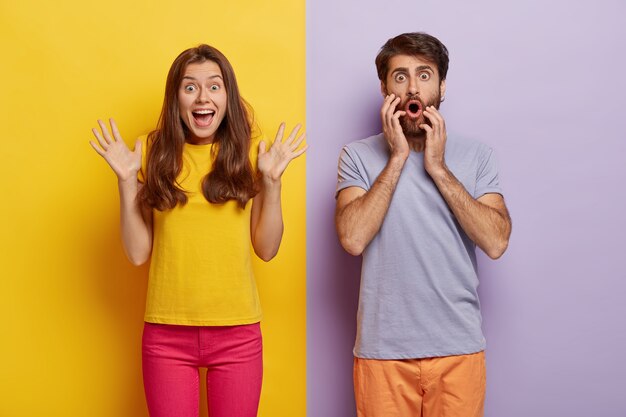 Photo of cheerful excited woman raises hands and exclaims something emotionally, shocked man stares with great wonder