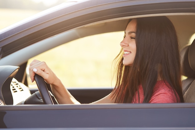 Photo of delighted glad brunette female driver looks happily at windscreen