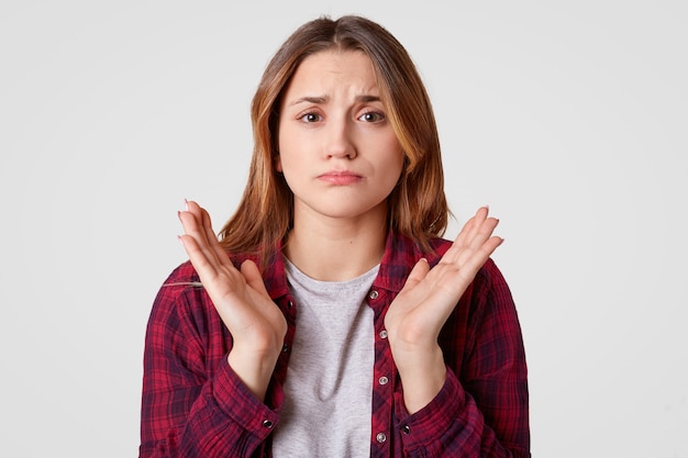 Photo of displeased European woman spreads palms, has pity facial expression, wears casual clothes, isolated over white wall, doubts about something. People, disappointment, dissatisfaction