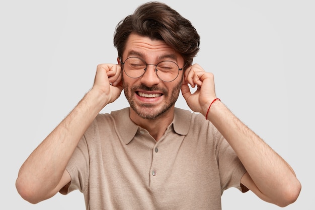 Photo of displeased man plugs ears with dissatisfaction, ignores someone