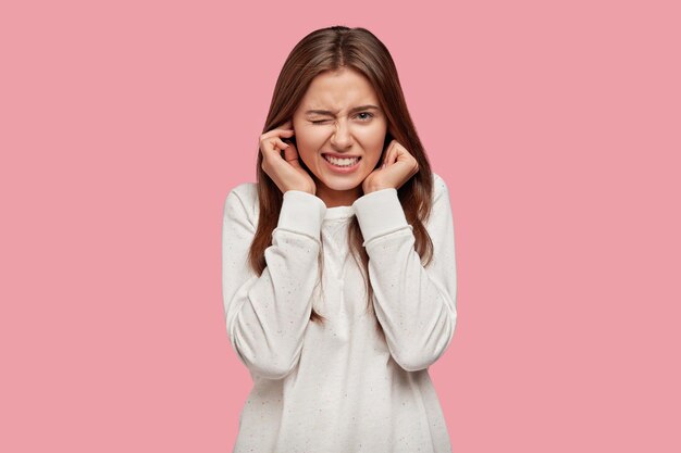 Photo of displeased woman plugs ears with discontent, doesnt want to hear annoying sound or noise