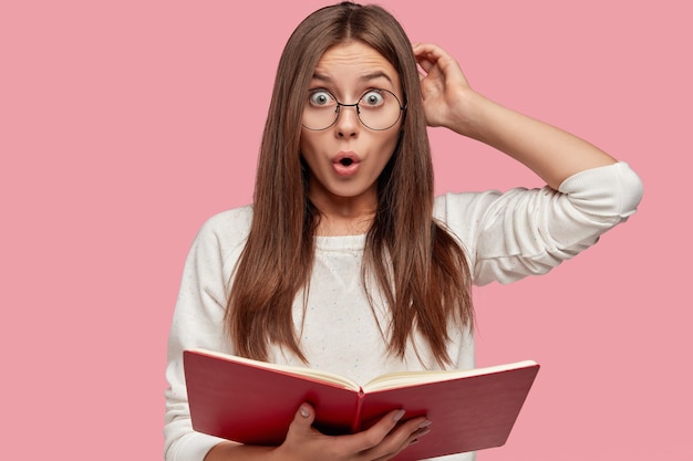 Photo of emotive surprised European girl scratches head with bewilderment