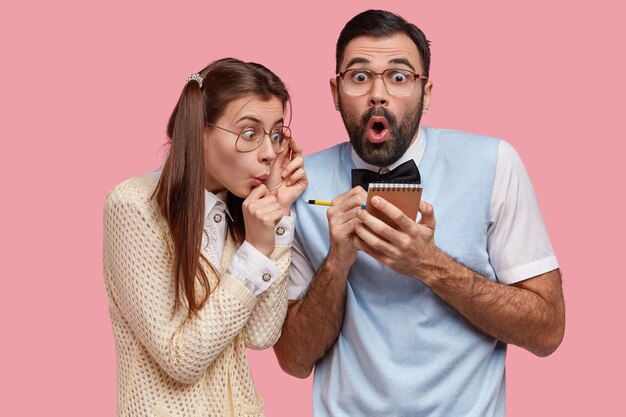 Free photo photo of fearful female and male nerds write down notes in spiral notepad, make records, surpised with list to do