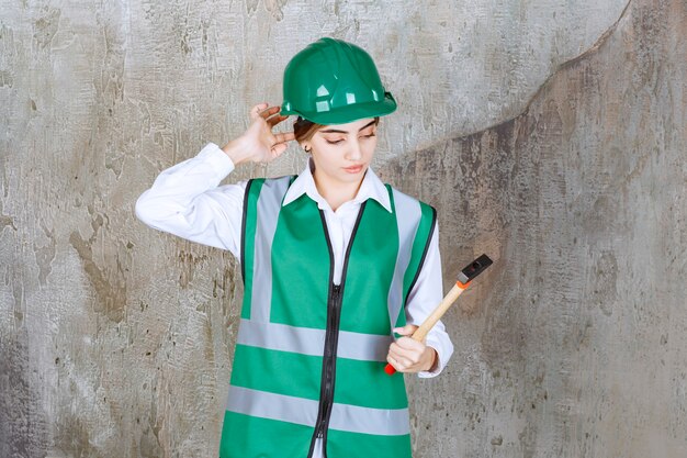 Photo of female construction worker in green helmet holding hammer